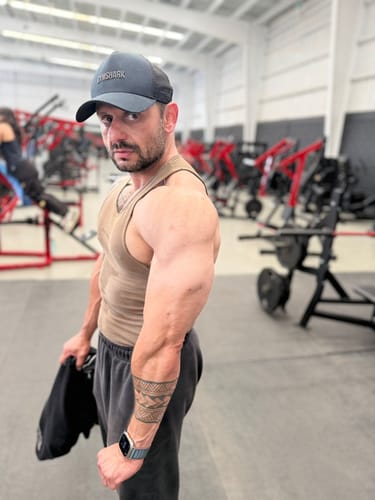 Usuario en un gimnasio mostrando su brazo musculoso y definido en una reseña de Stanoprime Winstrol.