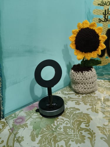 Customer's black 360° MagPro Magnetic Phone Holder standing on a patterned surface next to a decorative sunflower.