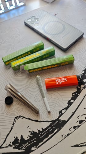 Customer's ROLLZ THCA Pre-Roll, its green packaging, and an orange lighter laid out on a desk mat.