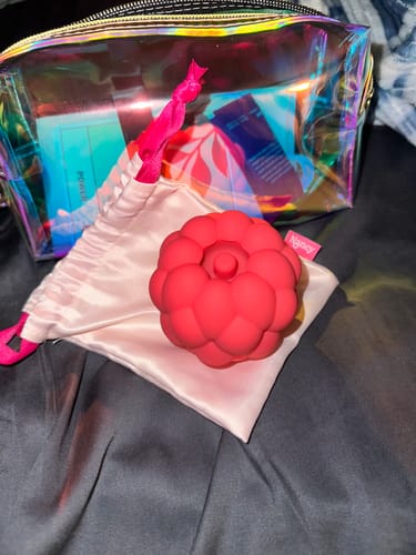 Customer's red Berri Tapping Clitoral Massager shown with its pink satin pouch on a bed.