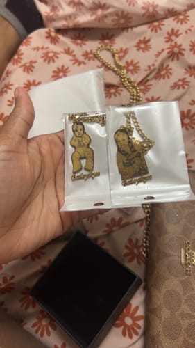 Reviewer holding two gold-colored photo engraved pendant necklaces, each in its own clear packaging.