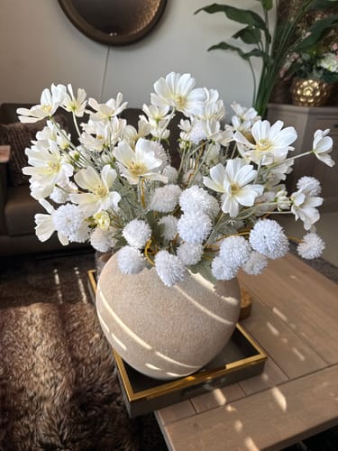Klant toont het volle, witte Boeket Serene in een ronde vaas op een salontafel.