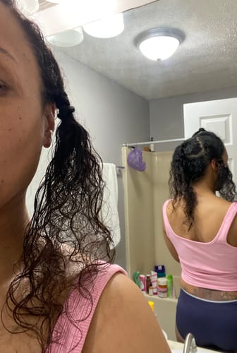 Reviewer showing a section of her long, curly hair loose before styling in a bathroom.
