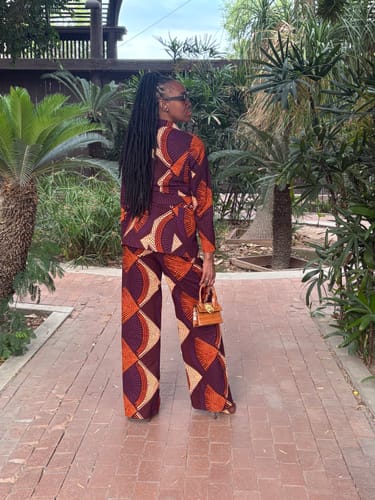 Reviewer from behind in the vibrant ZYLA AFRICAN PRINT SUIT SET on a brick path surrounded by tropical plants.