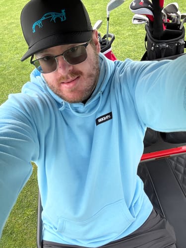 Reviewer taking a selfie wearing the black 80Eighty® Limited Edition DCG87 Hat on a golf course.