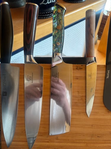 Kunde zeigt vier verschiedene Premium-Küchenmesser aus der Mystery Box auf einem Holzbrett.