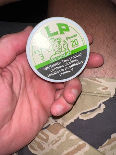 Customer holding a white and green can of LP Spearmint Nicotine Pouches in their hand.