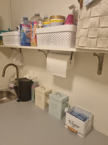 Anmelderens selvklebende tørkerullholder montert under en hylle på et vaskerom.