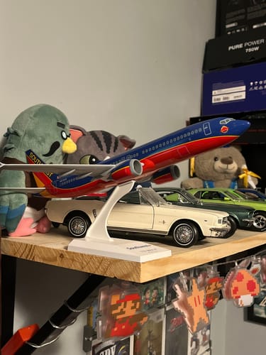 Reviewer's SKYMARKS SOUTHWEST 737-MAX8 model airplane on its stand, displayed on a wooden shelf with other collectibles.