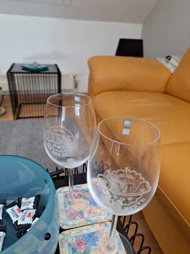 Kunde zeigt die beiden gravierten Leonardo Weingläser für Oma und Opa auf einem Tisch im Wohnzimmer.