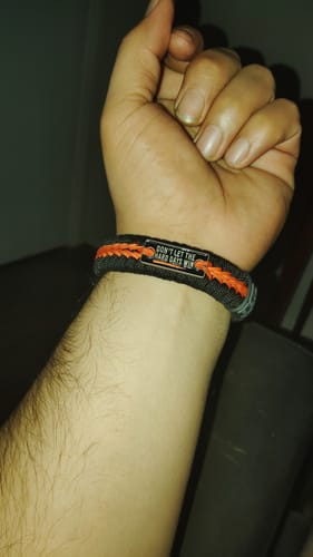 Customer's wrist wearing the Hard Days Paracord Bracelet, showing its grey and orange woven design and engraved metal plate.