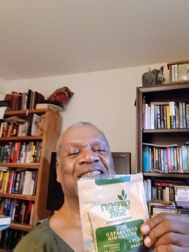 Reviewer smiling while holding a package of Green Salt in a room with bookshelves.
