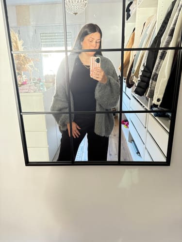 Kundin trägt den grauen, flauschigen Oversized Cardigan als Spiegelselfie über einem komplett schwarzen Outfit.
