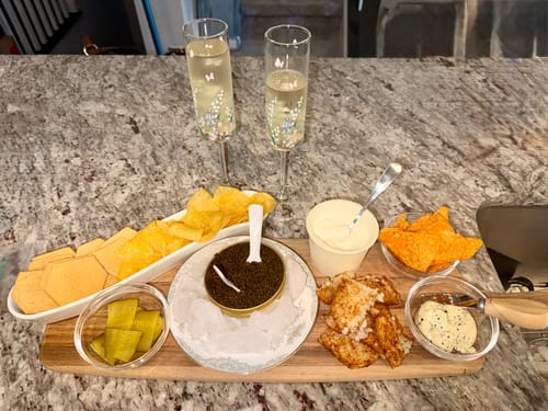Reviewer's Kaluga Hybrid Caviar served on a platter with crackers, dips, and champagne.
