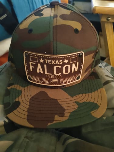 Customer's camouflage snapback hat with a custom Texas license plate patch reading 'FALCON'.