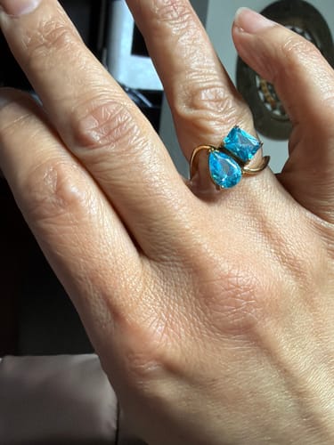 A customer's hand wearing the Navae Birthstone Ring with two bright blue stones on a gold-colored band.