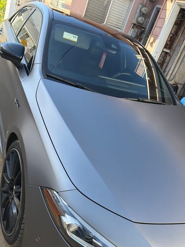Customer's red 80Eighty air freshener hanging from the rearview mirror of their matte grey car.