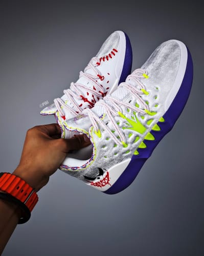 A reviewer holds a pair of Joker 2 "Wildcard" shoes, showing the detailed white, purple, and neon colorway.