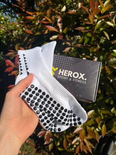 Recensore tiene in mano un paio di calze ProGrip® bianche, mostrando la suola con i grip neri e la scatola sullo sfondo.