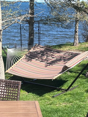 Customer's striped hammock with steel stand set up on a grassy lawn next to the water.