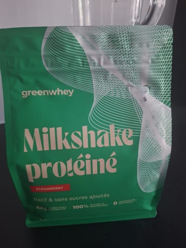 Un client montre le sachet vert du Milkshake Protéiné à la fraise, posé sur une table.