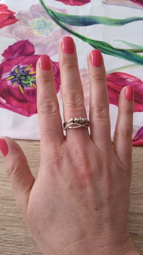 Kundin zeigt ihre Hand mit aufgetragenen, rosafarbenen Hot Ombré UV-Gel-Nägeln vor einem floralen Hintergrund.