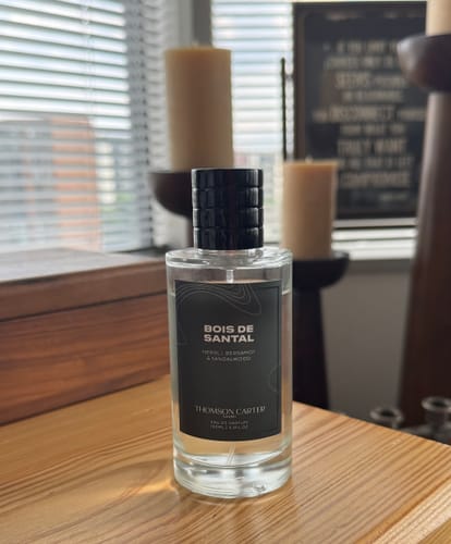 Reviewer's bottle of Bois De Santal Eau de Parfum sitting on a wooden surface in front of a window.
