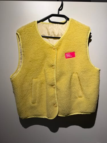 Rezensent zeigt die gelbe Teddy Weste, die an einem schwarzen Kleiderbügel hängt.