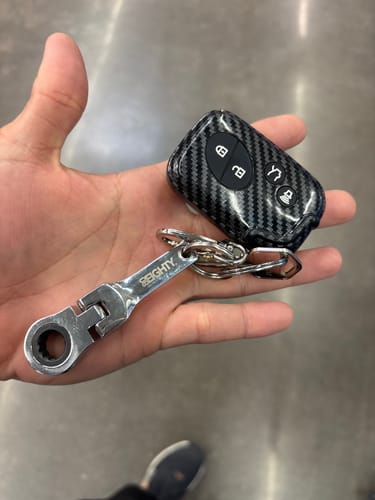 A customer's hand holding the shiny 80Eighty 10mm Wrench Keychain attached to a car key fob.