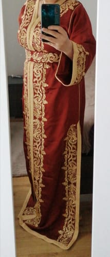 Customer wearing the Caftan Ritaj, a long red dress with intricate gold embroidery and a matching belt.