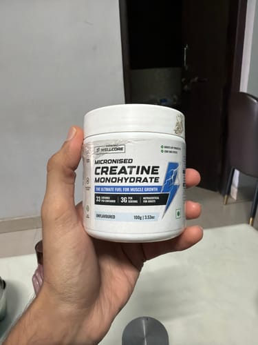 Customer holding a white tub of Wellcore Micronised Creatine Monohydrate indoors.