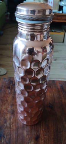 Customer's shiny copper water bottle with a textured honeycomb pattern on a wooden table.