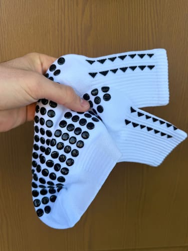 Un recensore tiene in mano un paio di calze ProGrip bianche, mostrando i gommini neri antiscivolo sulla suola.