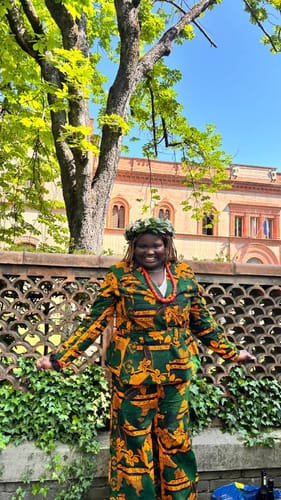 Reviewer smiling outdoors while wearing the ZYLA AFRICAN PRINT SUIT SET with a leafy wreath.