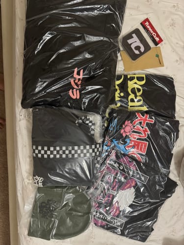 Customer displays the new apparel from their CULTIMATE MYSTERY CASH BOX, including packaged shirts, a hoodie, and a beanie.