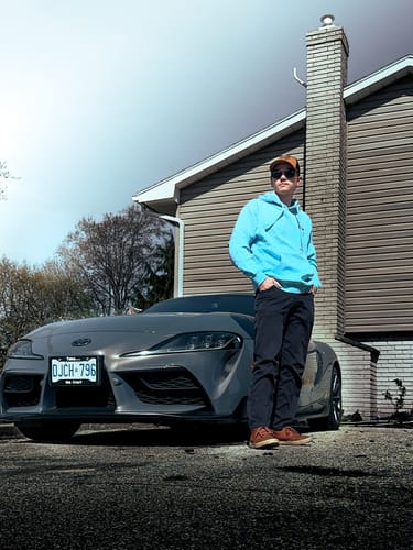 Customer wearing the light blue 80Eighty® DCG87 Hoodie in front of a modern gray sports car.