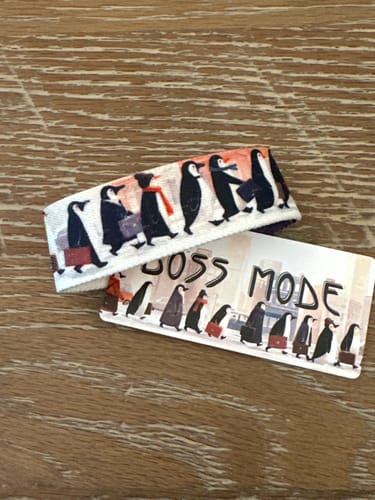Customer's Boss Mode Bracelet and matching card showing illustrated penguins dressed for work on a wooden surface.