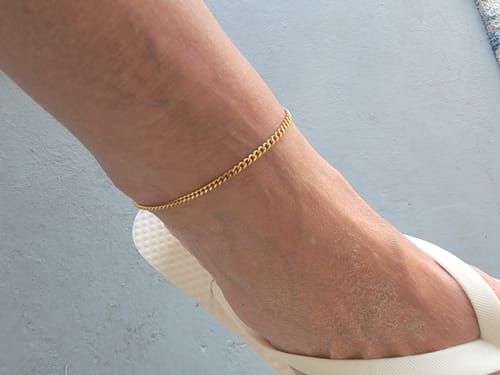 A customer wears the simple gold Miami Anklet on their ankle with a white flip-flop.