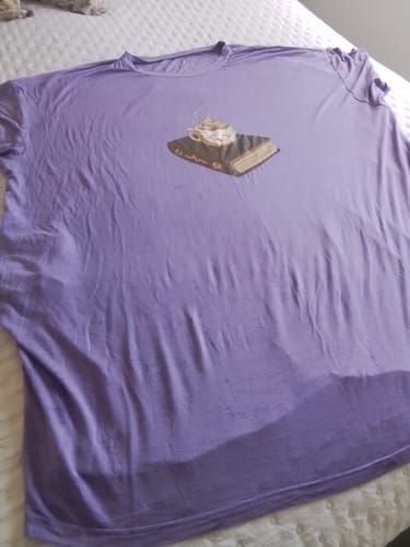Cliente mostrando a Camisola Livro lilás com uma estampa de livro, estendida sobre uma cama.