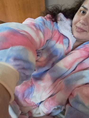 Cliente sorrindo enquanto relaxa com seu confortável cobertor vestível Sleepo Tie Dye.
