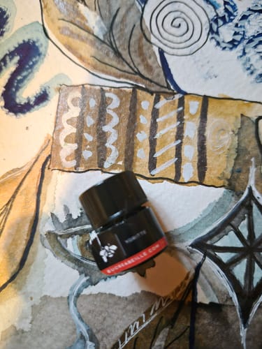 Reviewer's small sample bottle of Ygritte perfume resting on an artistic watercolor background.