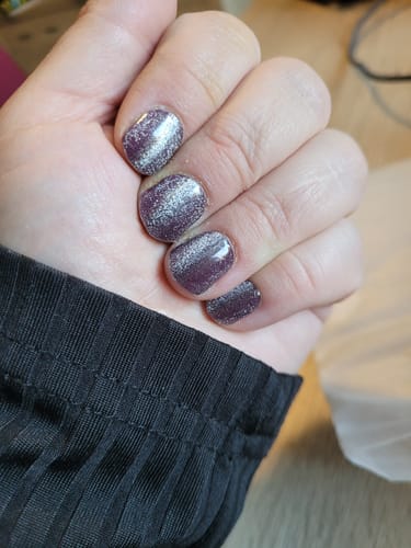 Nahaufnahme der Hand einer Kundin, die die glitzernden UV Gel Nagelfolien 'Burgundy Cateye' trägt.