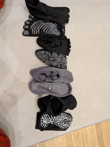 Reviewer's collection of various black and gray grip socks lined up on a floor.