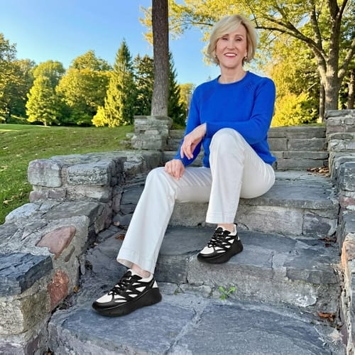Reviewer sitting on stone steps outdoors, wearing black and white Ortho Balance shoes with white pants.