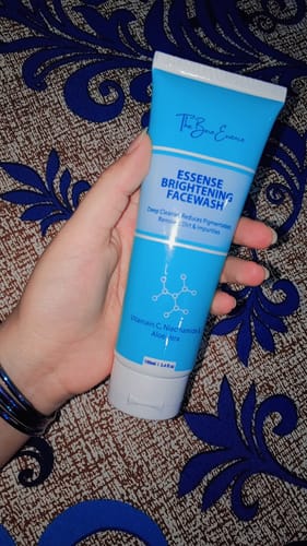 A reviewer holds the blue and white tube of Essense Brightening Facewash in their hand.