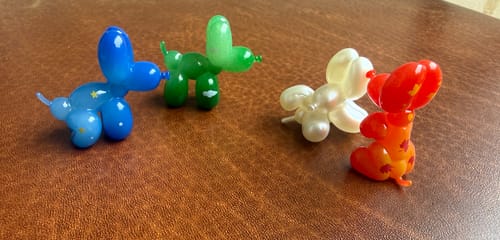 Customer's four glossy Happy Balloon Dog mini figures in blue, green, white, and orange on a brown surface.