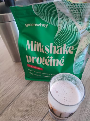 Photo d'un client montrant le sachet de Milkshake protéiné à la fraise à côté d'un verre de boisson rose et mousseuse.