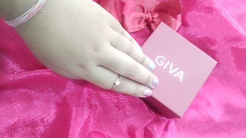 A reviewer's hand wearing the elegant Golden Star Constellation Ring next to the pink GIVA brand box on a pink background.