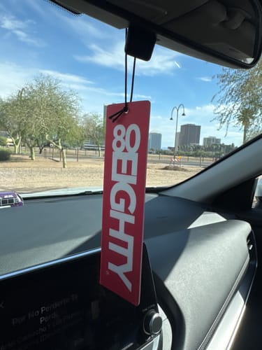Reviewer's red 80Eighty Air Freshener hanging from the rearview mirror of a car, seen from the dashboard.