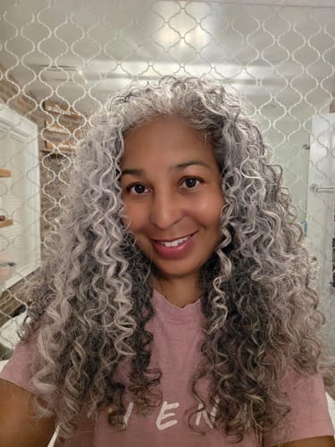 A reviewer with voluminous, defined gray curls smiling after using the CurlMix hair product.